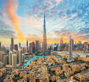 Stadtpanorama von Dubai mit dem Burj Khalifa im Zentrum, modernen Hochhäusern und Wasserflächen bei farbenfrohem Sonnenuntergang.