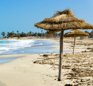 Strand mit Strohmsonnenschirmen auf Djerba, Tunesien.