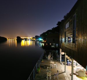 N&auml;chtliche Szene an der Donau mit beleuchteten schwimmenden Bars und Caf&eacute;s, Lichter spiegeln sich im ruhigen Wasser.