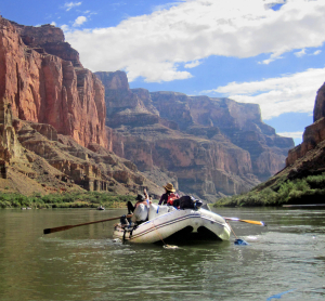 Ein Schlauchboot mit Abenteurern f&auml;hrt auf dem Colorado River zwischen den steilen, roten Felsw&auml;nden des Grand Canyon.