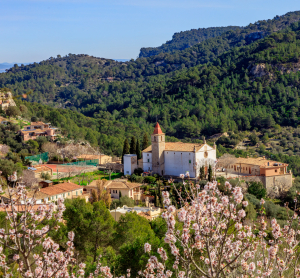 Bergdorf mit wei&szlig;er Kirche, umgeben von Mandelbl&uuml;ten und gr&uuml;nen H&auml;ngen.