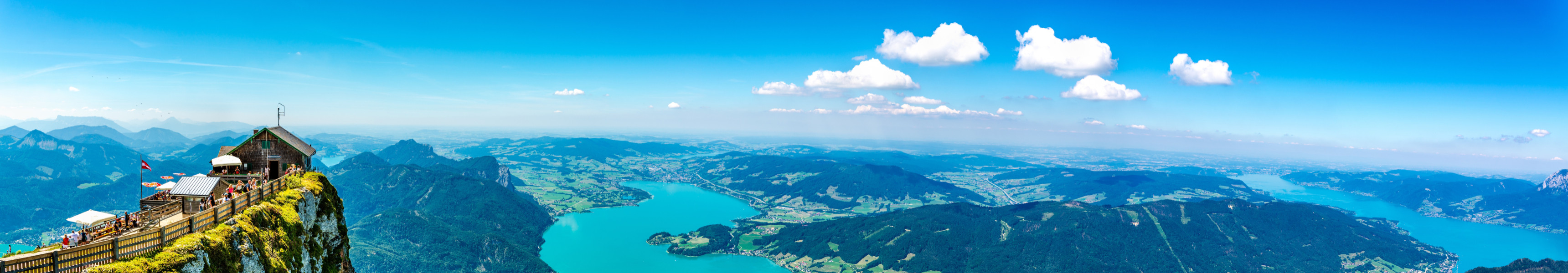 Blick vom Schafberg in &Ouml;sterreich auf das Salzkammergut mit einem Panorama von Bergen, Seen und gr&uuml;nen W&auml;ldern an einem klaren, sonnigen Tag.