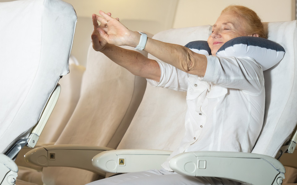 Tipps f&uuml;r entspanntes Fliegen: &Auml;ltere Frau dehnt und streckt sich am Platz 
