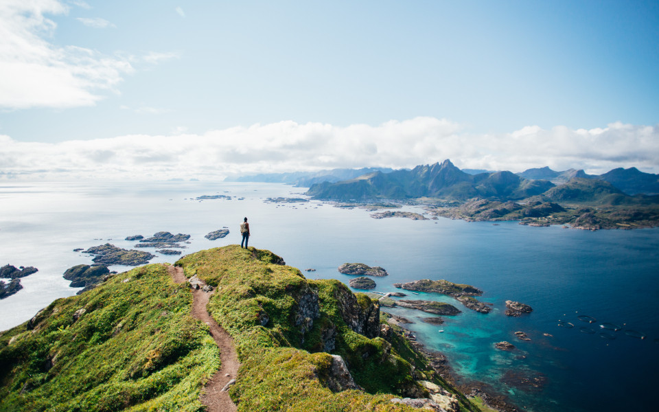 Erstaunliche epische Aufnahme eines jungen Wanderers, der nach einer langen, schwierigen Wanderung auf den Lofoten in Norwegen auf dem Gipfel eines Berges steht.
