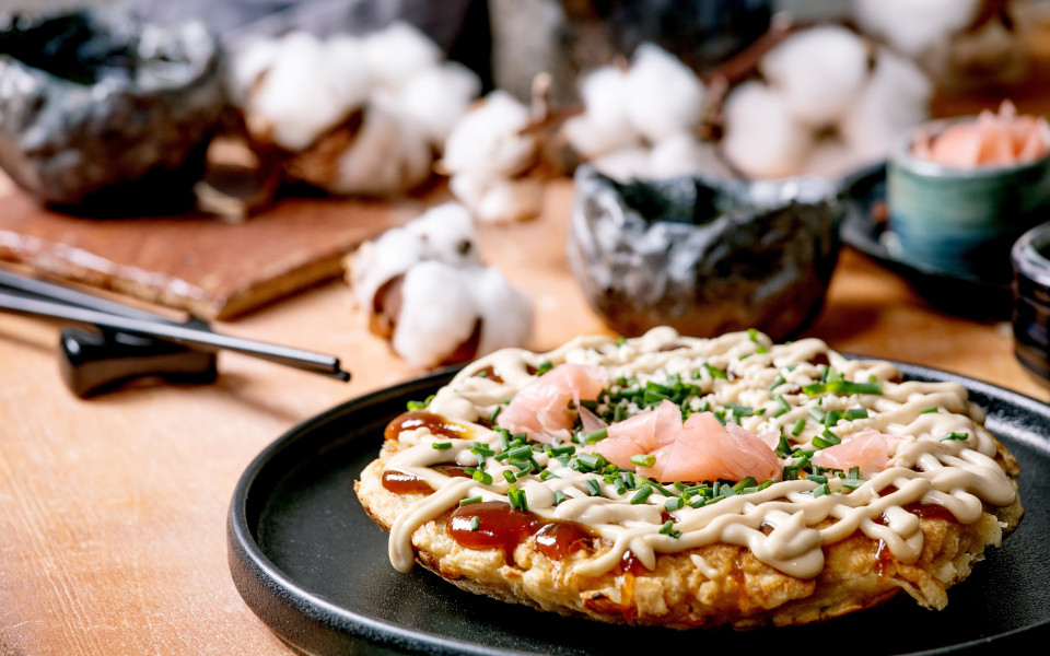 Hausgemachter japanischer Fastfood-Okonomiyaki-Kohlpfannkuchen mit Zwiebeln, eingelegtem Ingwer, Mayo-Sauce auf schwarzem Keramikteller. 