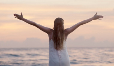 Frau streckt die Arme auseinander mit Blick auf das Meer